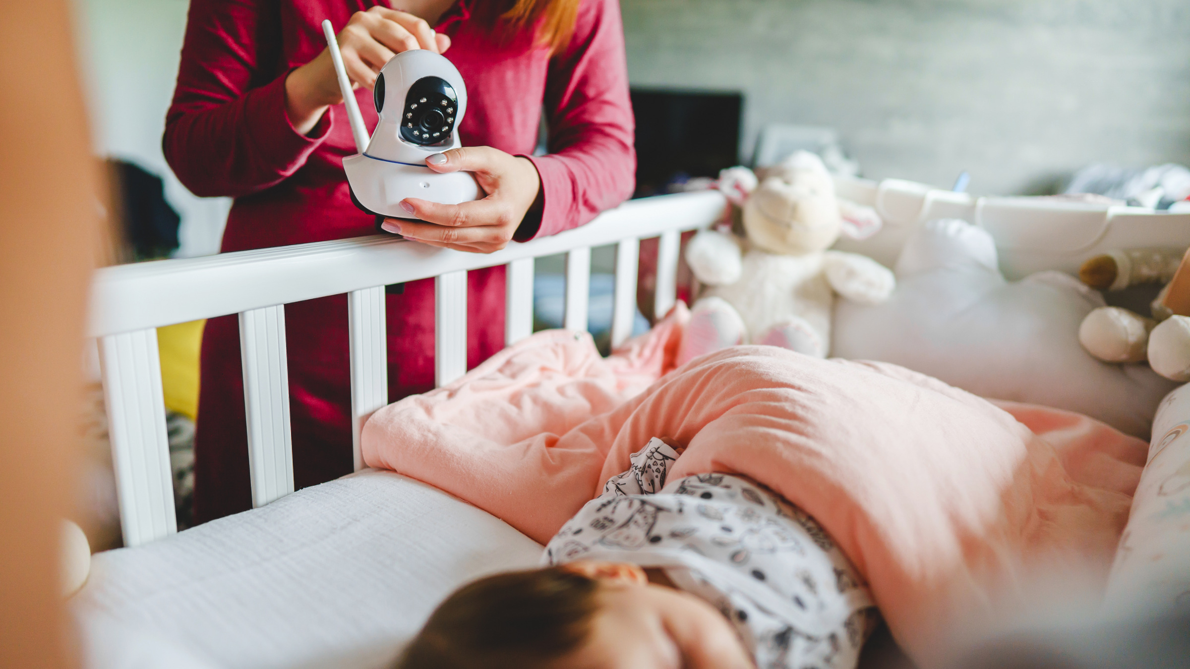 woman adjusting a baby monitor near bed of a sleeping child