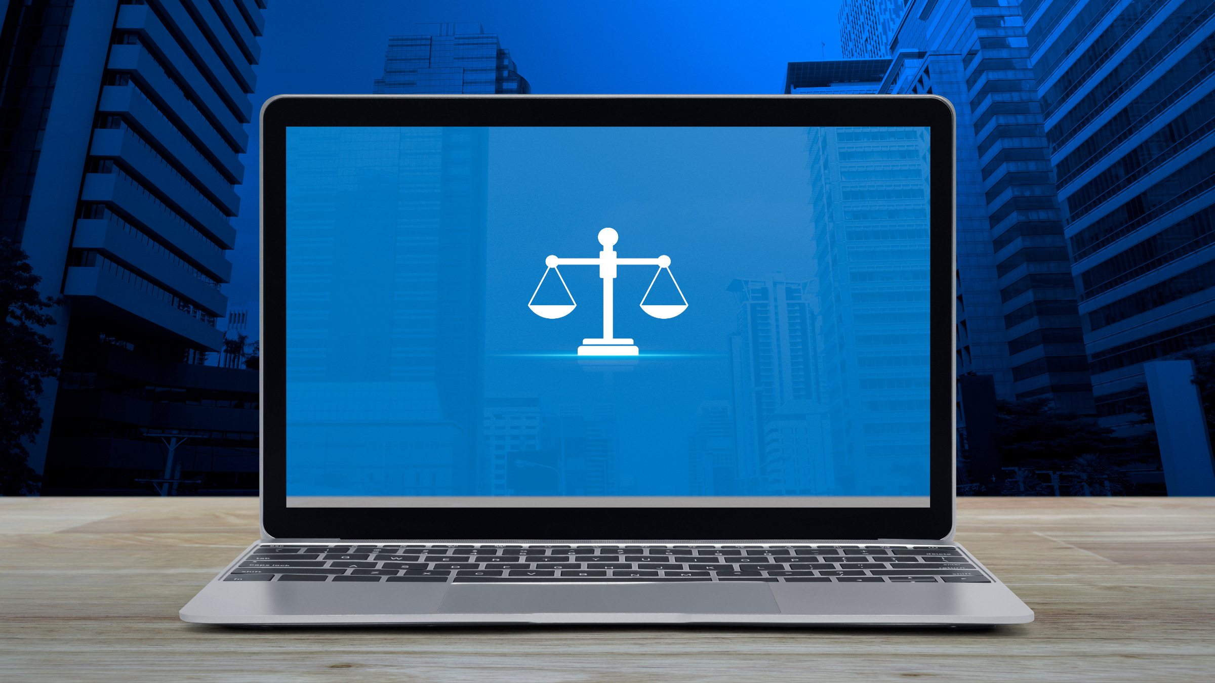 scales of justice on a computer screen on table with window and skyscrapers in the background